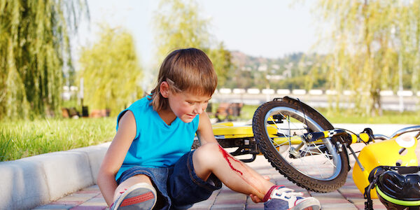 Crying boy with a bleeding injury sitting beside the bike that he has fallen from